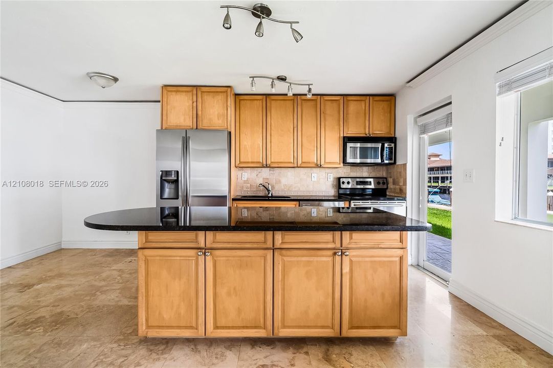 Kitchen featuring wood cabinetry, dark stone-finish countertops, an expansive center island, stainless steel appliances, and stone-tile flooring