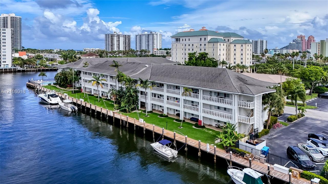 Multi-story residential complex featuring waterfront bulkhead, private boat slips, extensive manicured lawn, and paved parking area