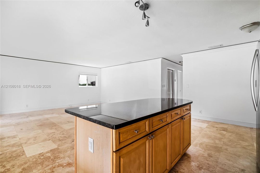 Central kitchen island featuring wood cabinetry and a dark stone countertop, complemented by natural stone-finish floor tiling and multi-directional track lighting