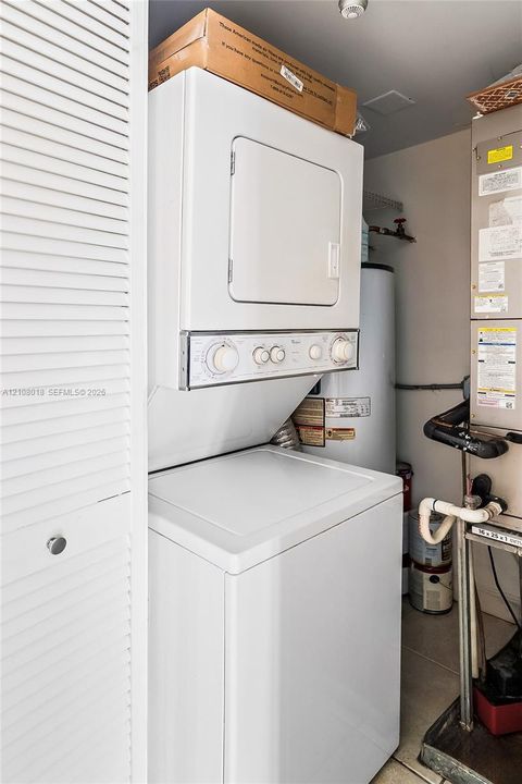 Utility closet featuring a stacked washer and dryer, cylindrical water heater, and HVAC unit, enclosed by white louvered doors