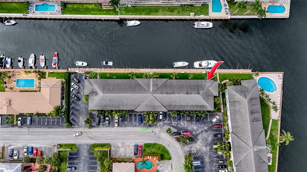 Aerial perspective of waterfront property featuring a concrete seawall, direct waterway access, private boat dockage, and paved surface parking