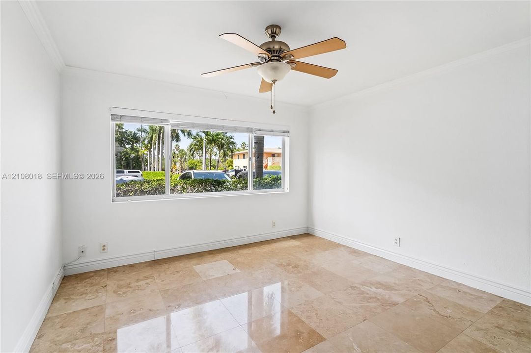Interior space featuring polished natural stone flooring, a multi-blade ceiling fan with integrated lighting, crown molding, and a large window