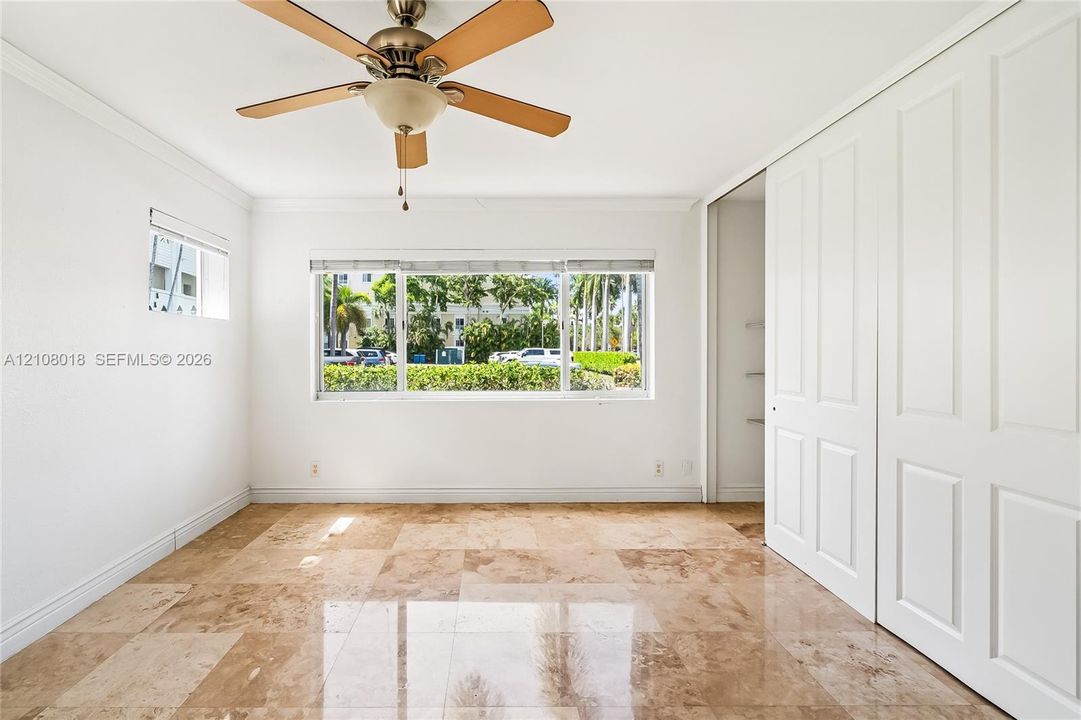 Polished stone flooring, ceiling fan with integrated light fixture, large picture window, and floor-to-ceiling closet with paneled sliding doors