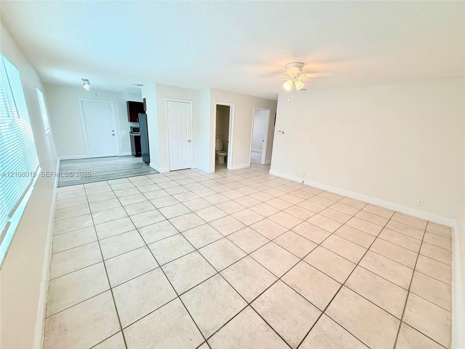 Neutral-toned interior featuring large-format square tile flooring, a ceiling-mounted light fixture with fan, and multi-pane horizontal blinds