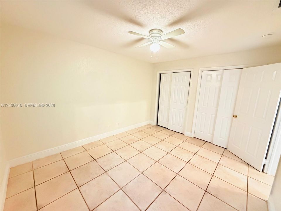 Neutral-toned ceramic tile flooring, dual sets of white closet doors, and a ceiling fan with integrated lighting