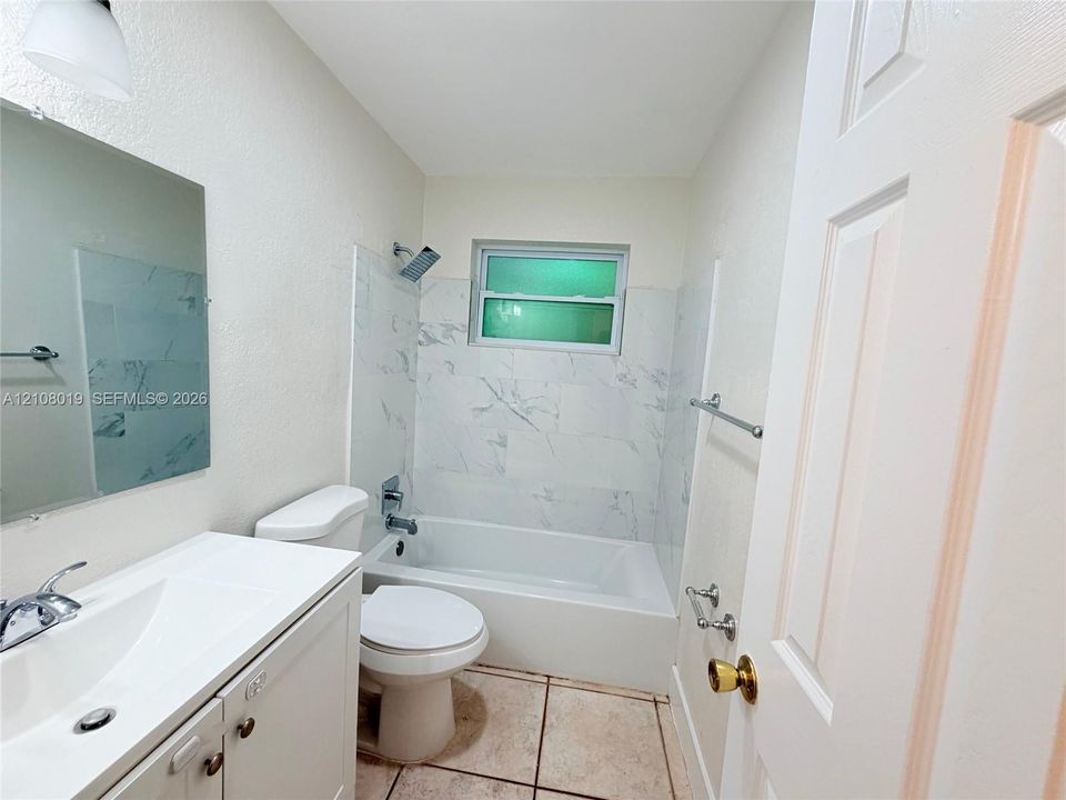 Bathroom featuring a vanity with a white integrated sink, polished chrome faucet, rectangular wall-mounted mirror, and a tub-shower combination with light-toned, stone-patterned wall tile