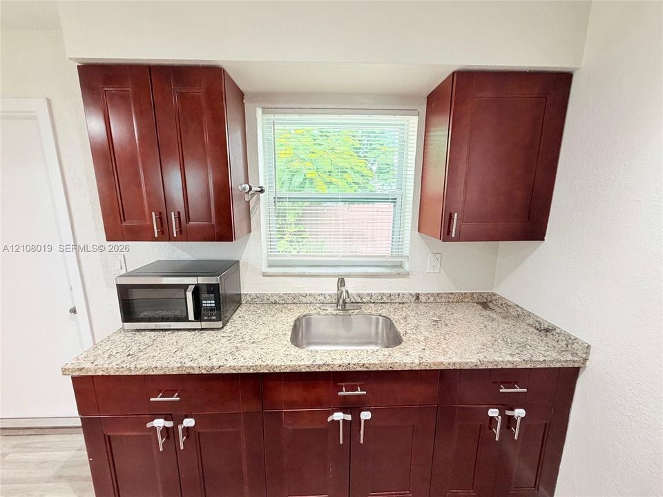 Kitchen featuring dark wood-finish cabinetry, stone-finish countertops, stainless steel undermount sink, and a high-arch faucet