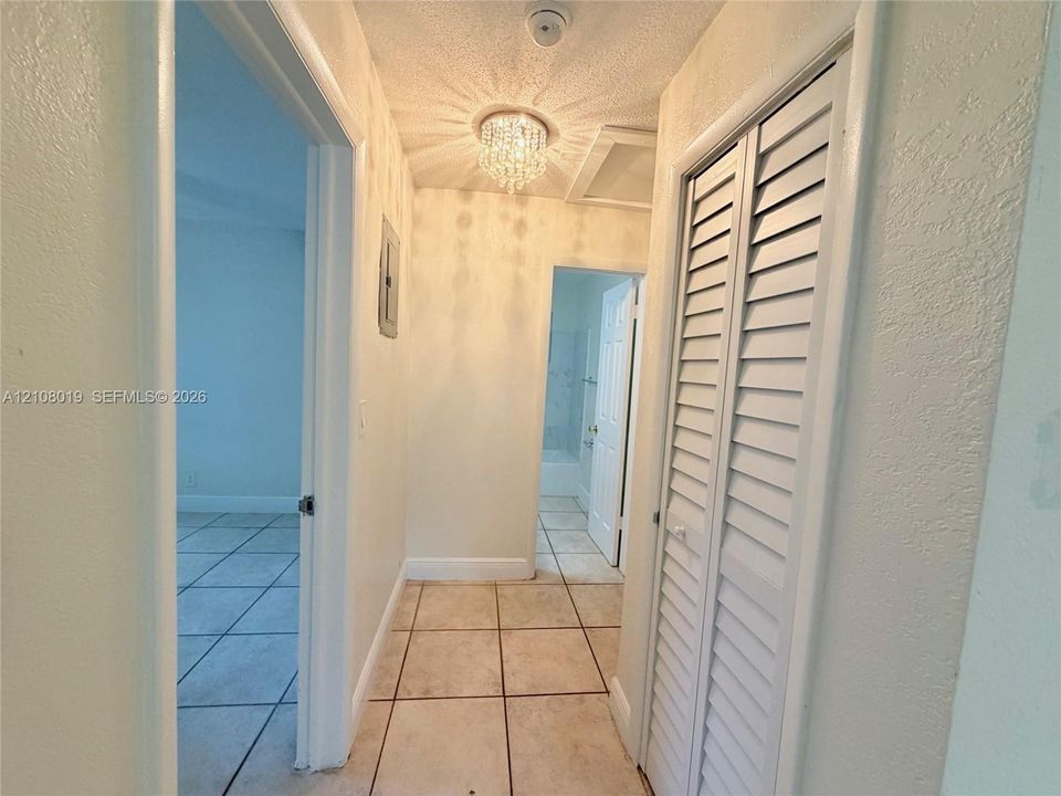 Hallway featuring ceramic tile flooring, a crystal-style flush mount light fixture, and white louvered-panel closet doors