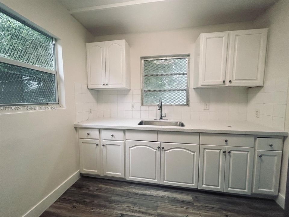 Kitchen featuring white cabinetry, solid-surface countertops, stainless steel sink with a high-arc faucet, white tile backsplash, and wood-finish flooring