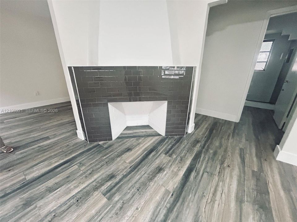 Fireplace featuring a dark glossy tile surround and wood-finish flooring throughout