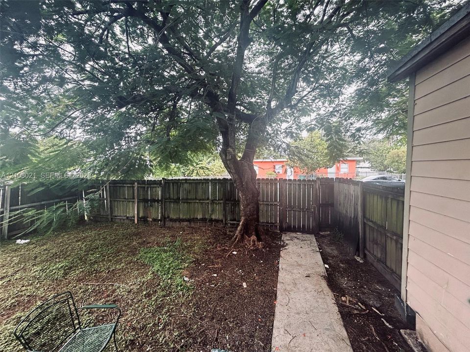 Rear exterior space featuring a concrete pathway, mature tree, and wood privacy fencing