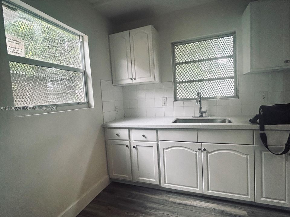 White cabinetry featuring recessed-panel doors, solid surface countertops, stainless steel sink with high-arc faucet, tile backsplash, and wood-finish flooring