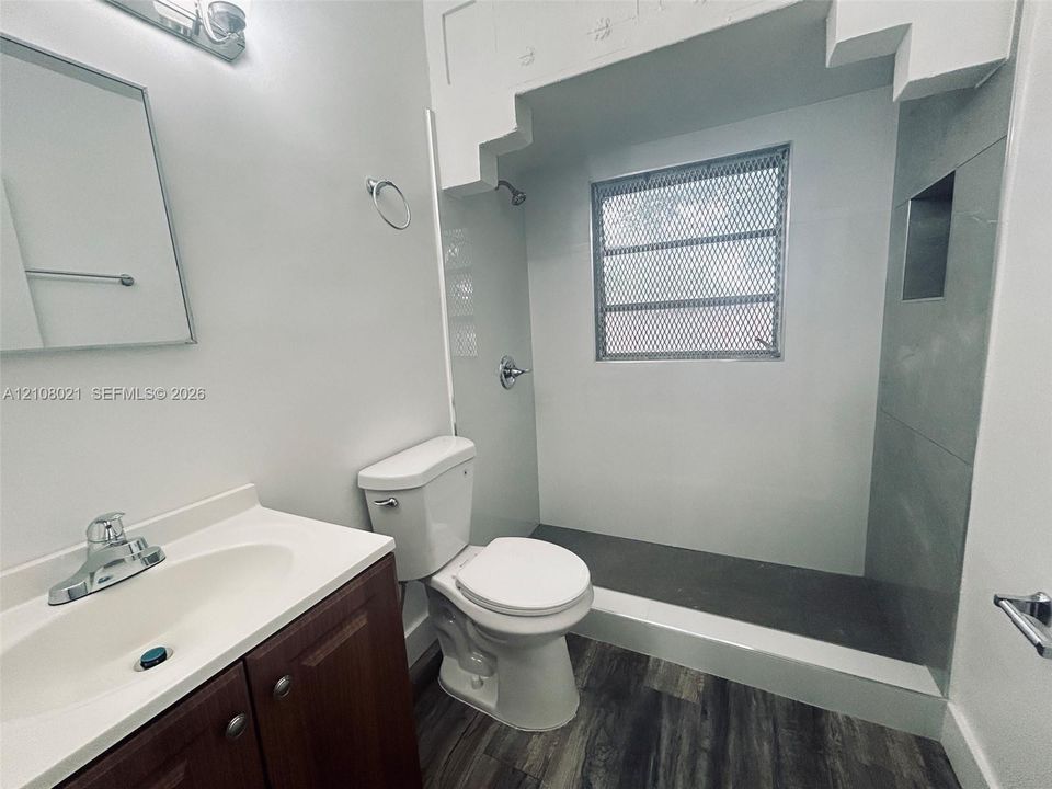 Bathroom featuring a wood-finish vanity, integrated sink, walk-in tiled shower with a built-in recessed shelf, and wood-finish flooring