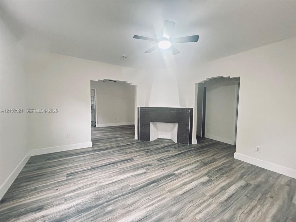 Interior featuring wood-finish flooring, a central fireplace with dark tile surround, stepped architectural archways, and a multi-blade ceiling fan with integrated lighting