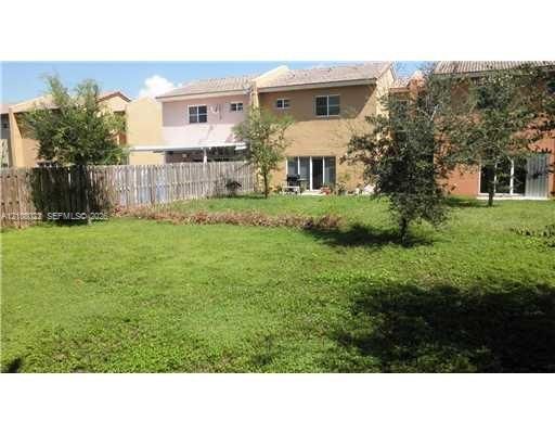 Expansive grassy backyard featuring a wooden privacy fence, mature trees, and ground-level rear access via sliding glass doors