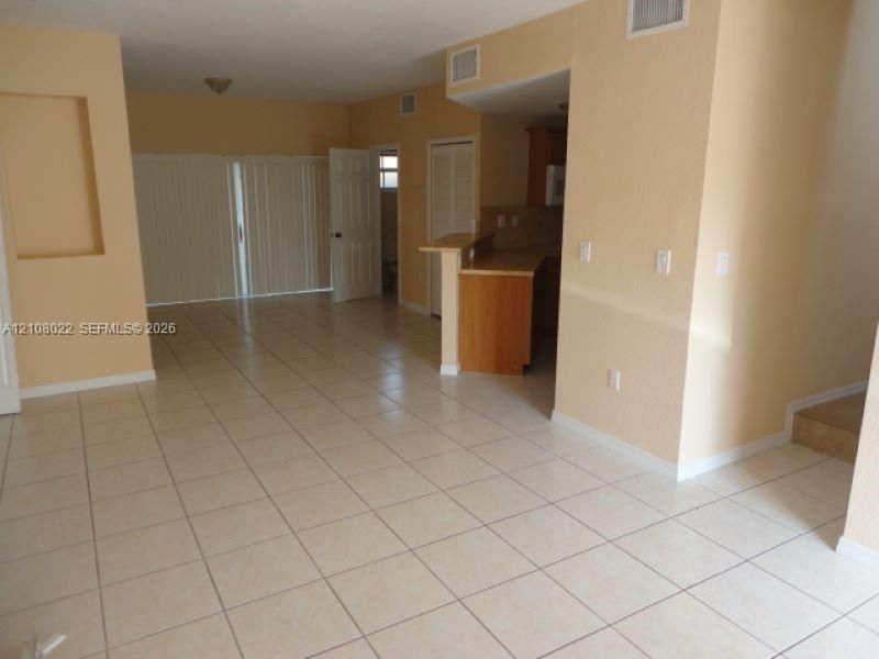 Open-concept interior featuring neutral tile flooring, built-in wall niche, kitchen breakfast bar, and vertical sliding door blinds