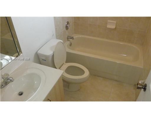 Bathroom featuring an integrated vanity countertop with an oval basin, chrome-finish faucet, tile-surround bathtub, and neutral-tone floor tiling