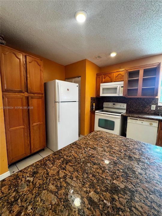 Kitchen featuring natural wood cabinetry, stone-finish countertops, and an integrated appliance suite including a built-in microwave