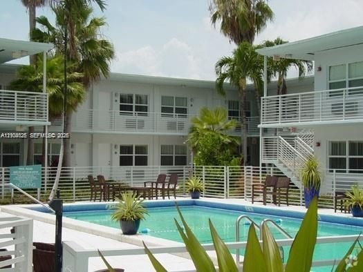 In-ground swimming pool with a white concrete deck, enclosed by a white metal perimeter fence, and surrounded by mature palm trees