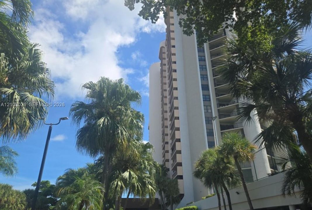 High-rise residential exterior featuring a multi-story concrete facade with recessed balconies and mature landscaping