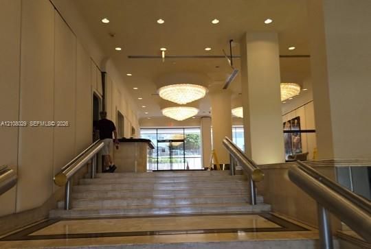 Entryway featuring stone steps, dual metallic handrails, recessed ceiling lighting, and tiered crystal chandeliers