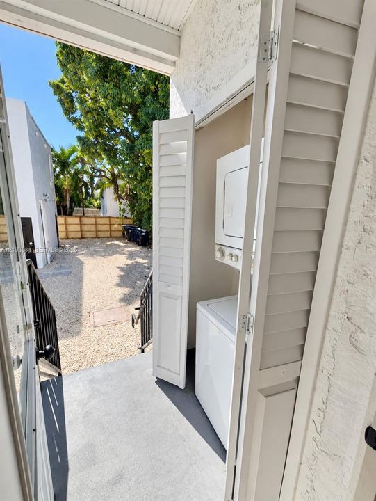 Laundry closet featuring folding louvered doors, stacked laundry appliances, and concrete flooring