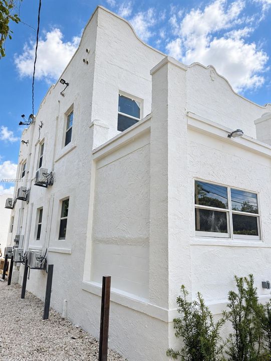 Exterior facade featuring white textured stucco finish, decorative curvilinear roofline, multi-pane windows, and wall-mounted exterior lighting