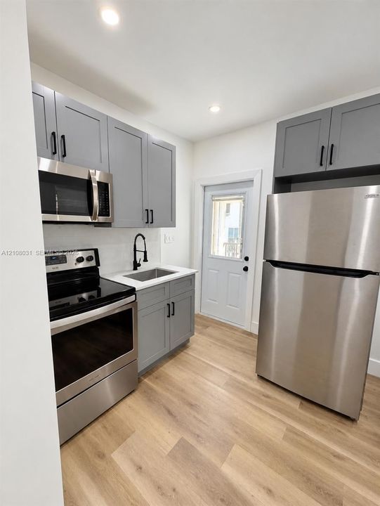 Kitchen featuring shaker-style grey cabinetry, stainless steel appliances, wood-finish flooring, quartz-surround countertops, and a matte black gooseneck faucet