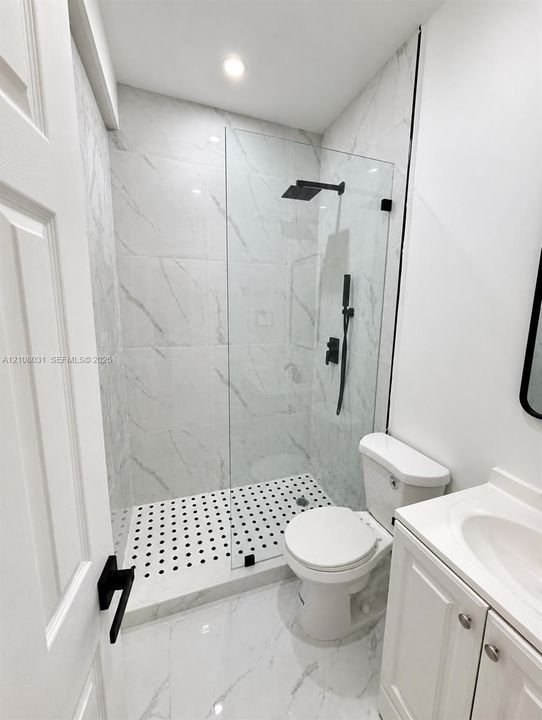 Walk-in shower featuring large-format stone-patterned tile, a frameless glass enclosure, a matte black rainfall showerhead with a handheld sprayer, and a contrasting circular-patterned mosaic tile floor