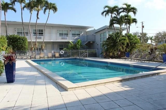 Rectangular swimming pool featuring a tile surround, metal perimeter fencing, and mature palm trees