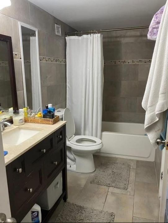 Dark-finished vanity with an integrated sink and neutral countertop, large-format tile flooring, and full-height wall tiling featuring a decorative mosaic inlay surrounding the tub and shower area