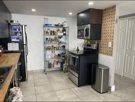 Kitchen featuring wood-surface countertops, tile flooring, recessed lighting, and stainless steel appliances including a range and microwave