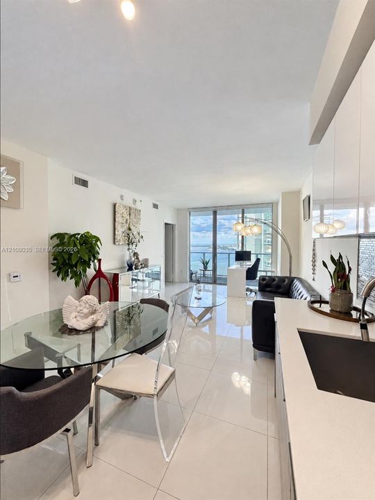 Open-concept living space featuring high-gloss cabinetry, stone countertops, large-format tile flooring, and floor-to-ceiling glass doors opening to a balcony