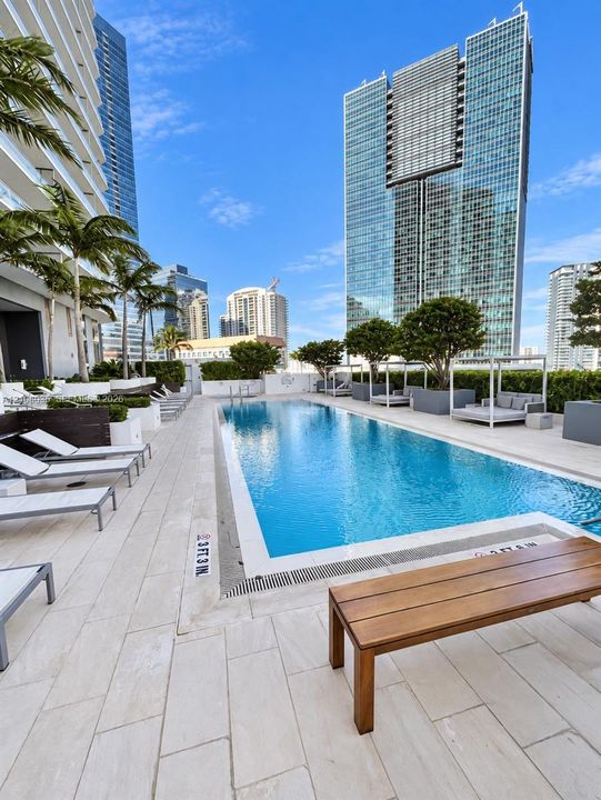 Swimming pool featuring light-toned stone decking, mature landscaping, and built-in privacy hedges