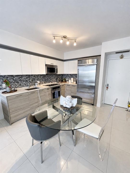Modern kitchen featuring high-gloss white upper cabinetry, wood-finish base cabinetry, a mosaic tile backsplash, integrated stainless steel appliances, and large-format tile flooring