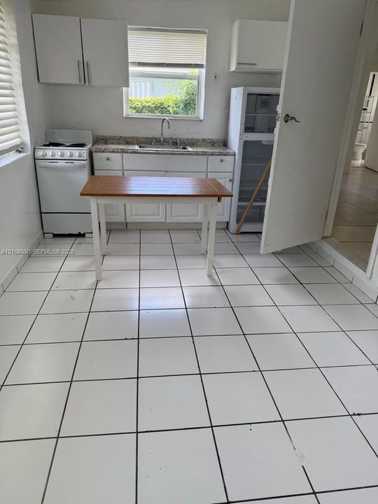 Kitchen featuring white cabinetry, stone-finish countertops, ceramic tile flooring, and a window over the stainless steel sink