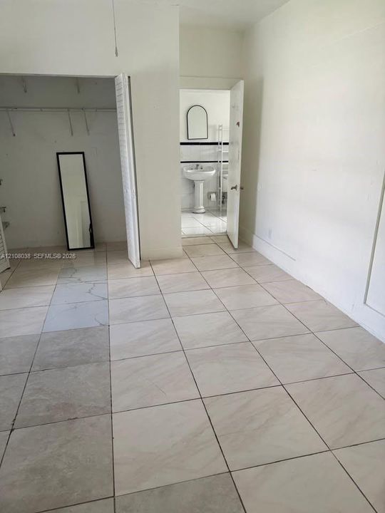 Neutral large-format tile flooring, built-in bi-fold closet, and pedestal sink with arched wall-mounted mirror