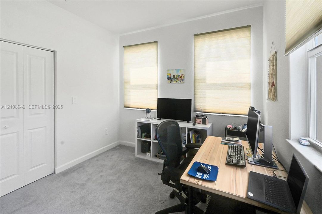 Interior room featuring neutral wall-to-wall carpeting, dual-panel closet doors, and three windows fitted with light-filtering cellular shades