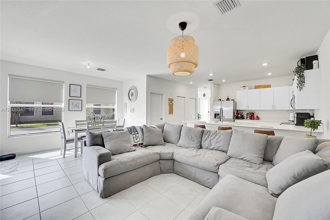 Open-concept interior featuring light-toned tile flooring, recessed lighting, a woven pendant light fixture, and white cabinetry