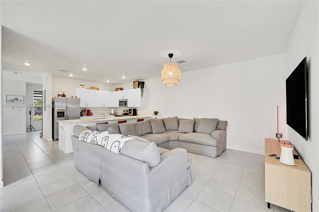 Open-concept space featuring large-format tile flooring, recessed lighting, white cabinetry, stainless steel appliances, and a central kitchen island