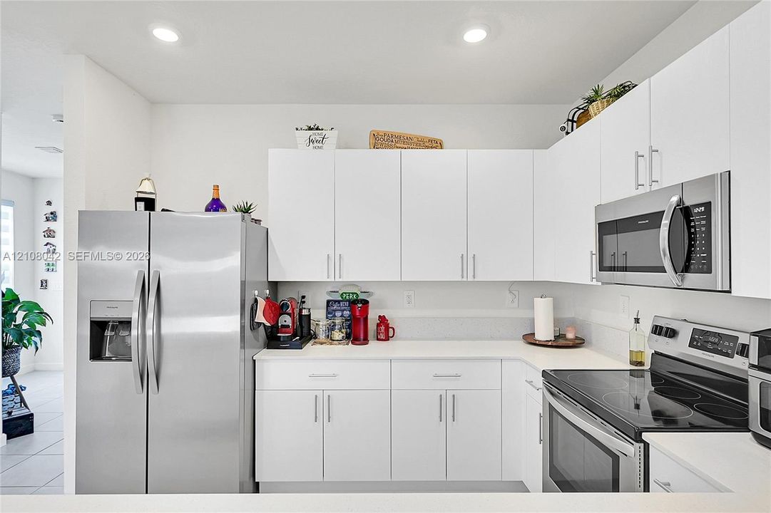 Kitchen featuring white cabinetry, solid-surface countertops, recessed ceiling lighting, and stainless steel appliances including a side-by-side refrigerator, over-the-range microwave, and electric range