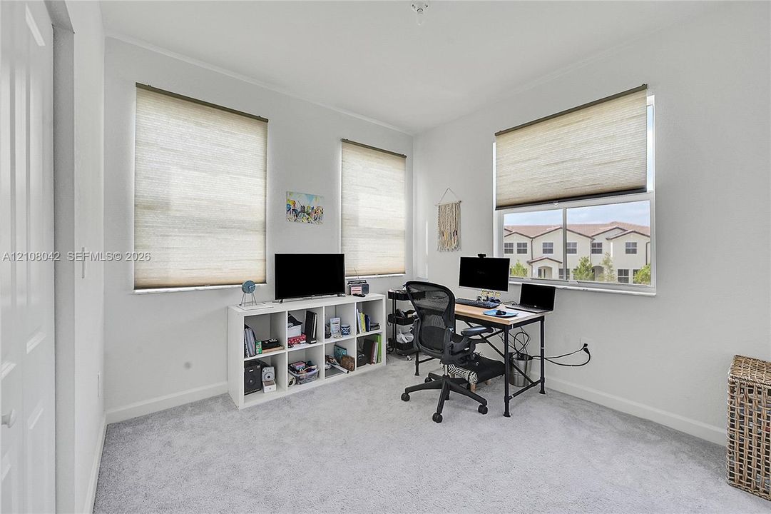 Neutral interior room featuring wall-to-wall carpeting, three multi-pane windows, and neutral roller shades