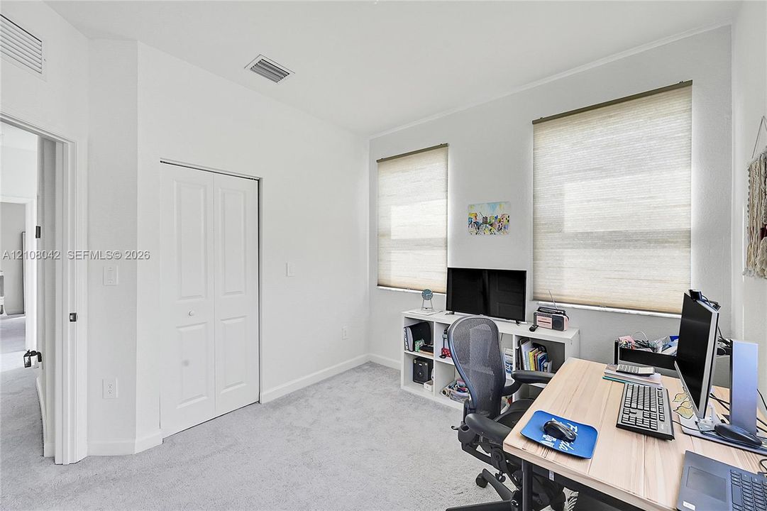 Neutral-toned interior space featuring light carpeting, dual windows with fitted roller shades, and a white double-door closet