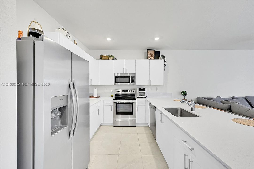 Kitchen featuring white cabinetry, solid-surface countertops, stainless steel appliances, a double-basin stainless steel sink, and tile flooring