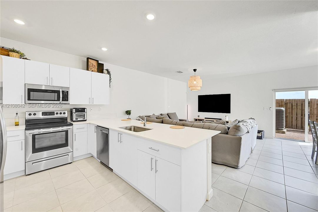 Kitchen featuring white cabinetry, quartz countertops, stainless steel appliances, a center island with an integrated sink, and tile flooring