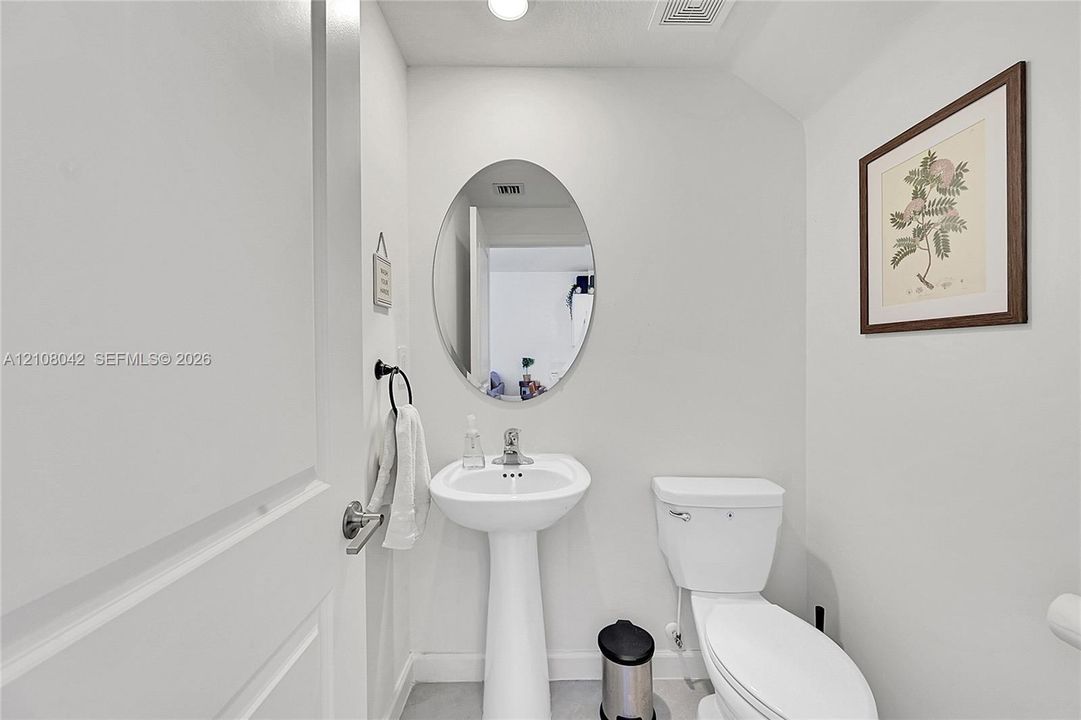 Pedestal sink with chrome faucet, oval wall-mounted mirror, and white commode