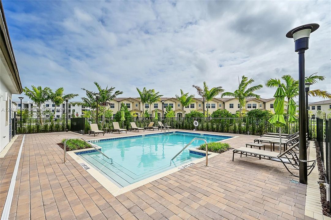 Swimming pool with blue tile border, paved deck, metal handrails, and surrounding palm trees
