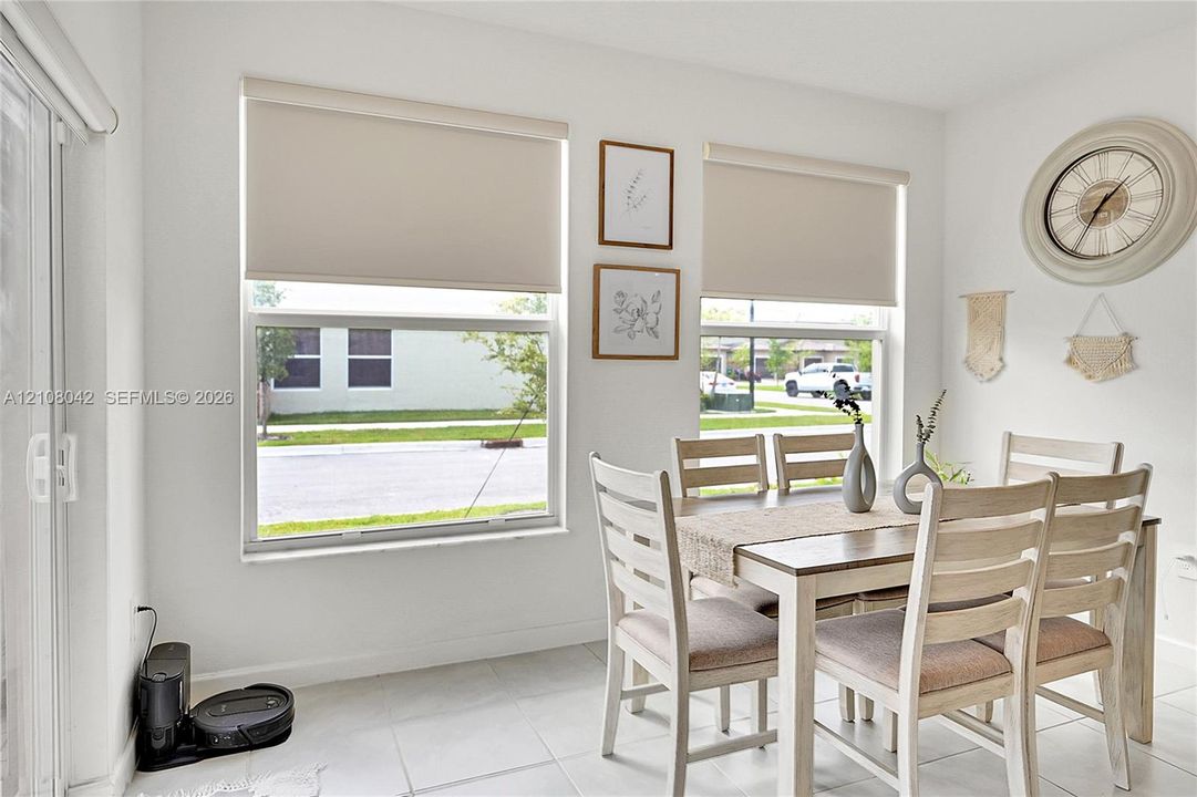 Neutral-toned space featuring large windows with roller shades, tile flooring, and a sliding glass door