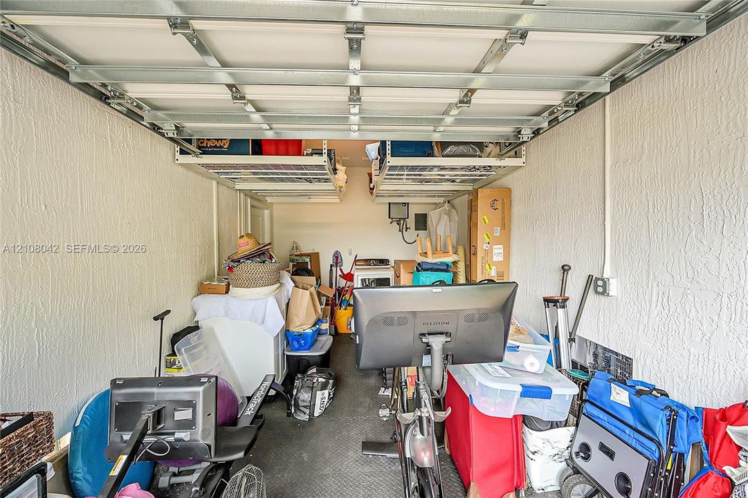 Garage interior featuring textured wall finishes, overhead metal storage racking systems, and a high-clearance sectional door mechanism