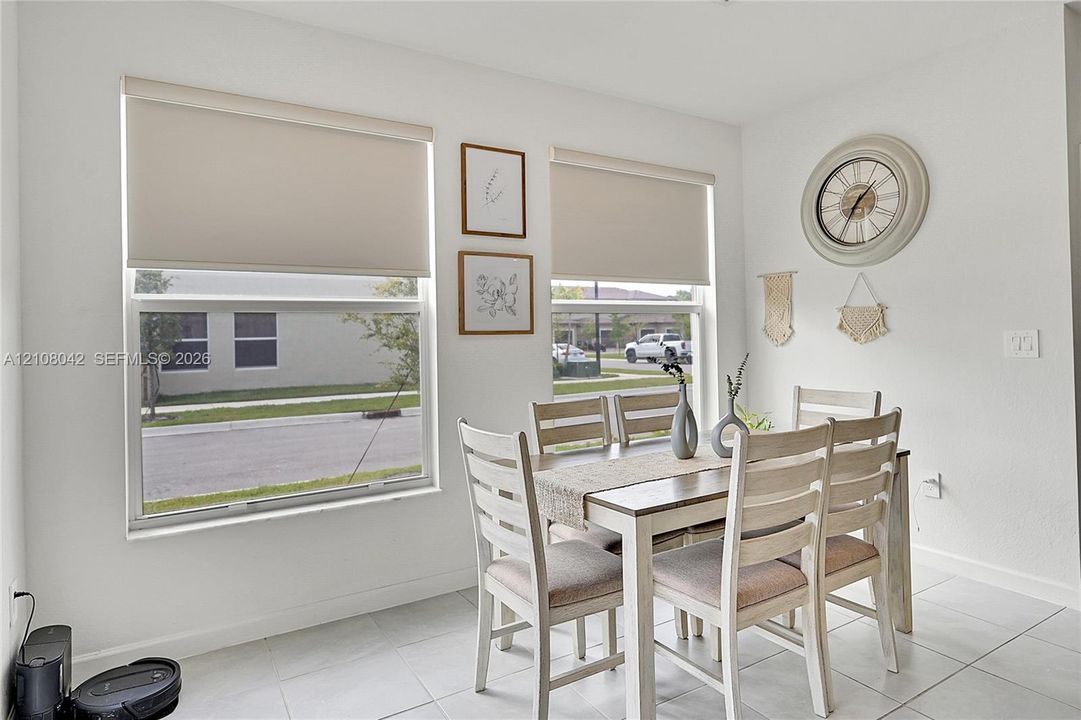 Bright interior space featuring large, dual-paned windows, neutral wall finishes, fitted roller shades, and light-toned tile flooring